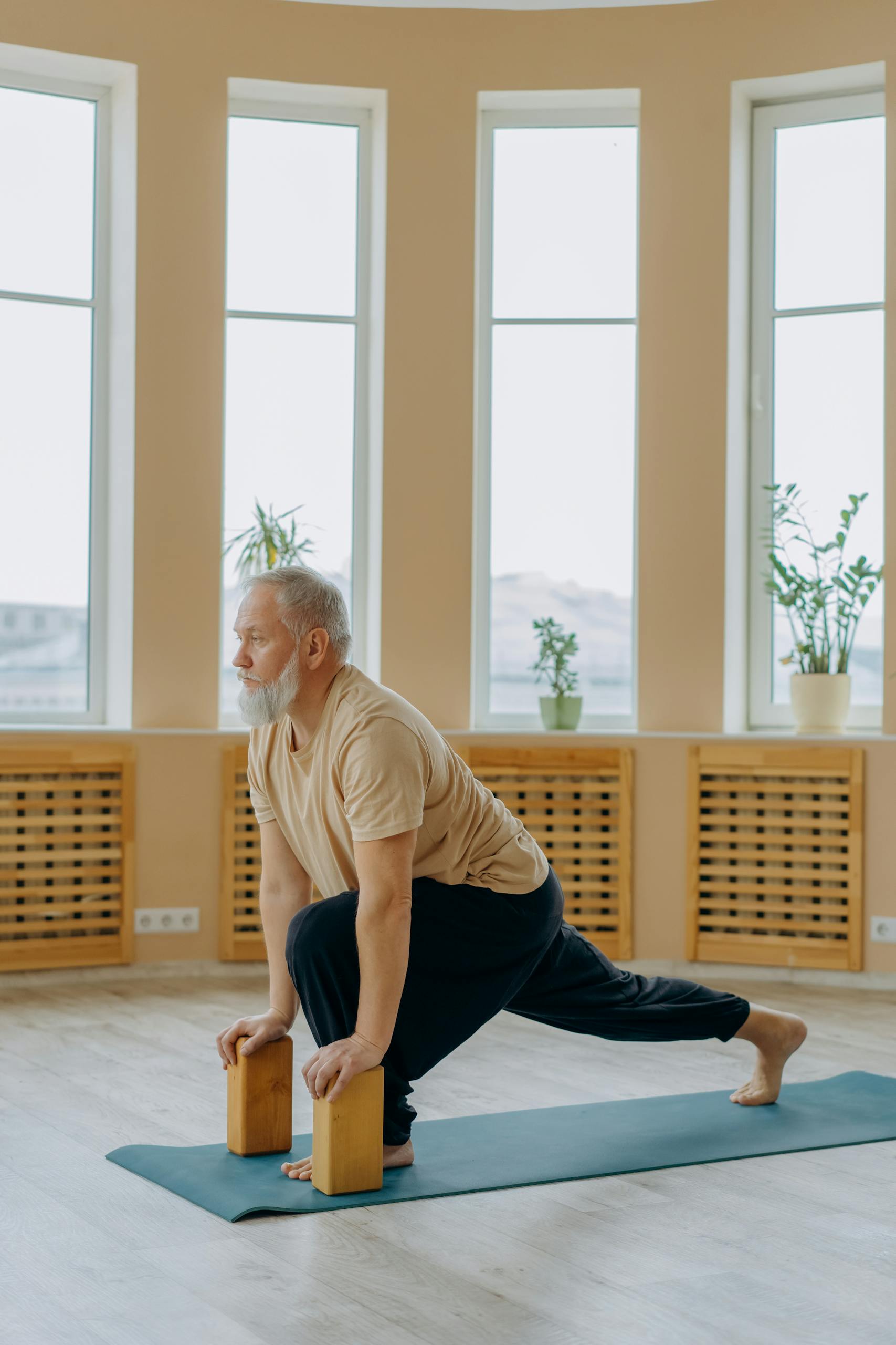 Senior man practicing yoga indoors using blocks for balanced wellness and healthy living.