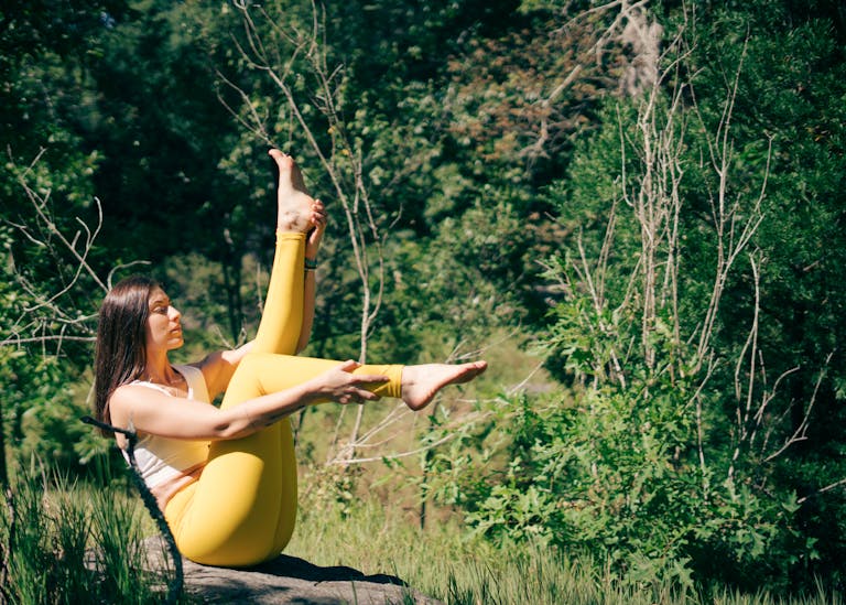A woman in yellow leggings practices yoga outdoors surrounded by lush greenery.